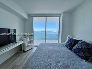 bedroom featuring a water view, expansive windows, and wood finished floors