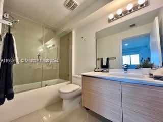 full bathroom featuring vanity, tile patterned flooring, combined bath / shower with glass door, and toilet