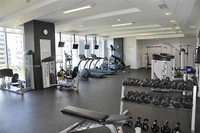 gym with a tray ceiling, expansive windows, and visible vents