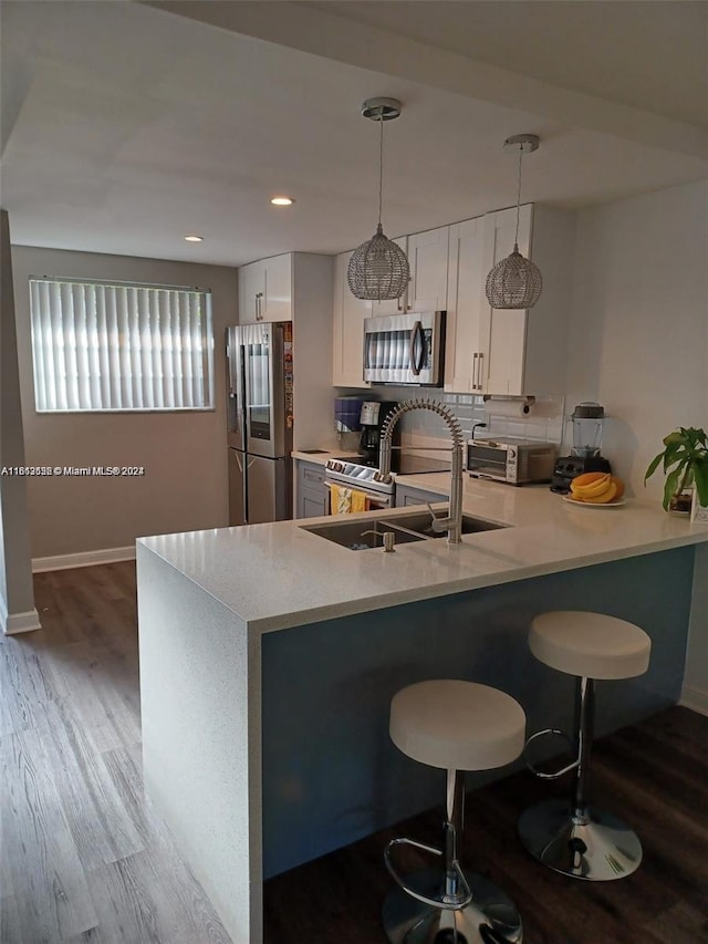 kitchen with white cabinetry, kitchen peninsula, light hardwood / wood-style flooring, appliances with stainless steel finishes, and decorative light fixtures