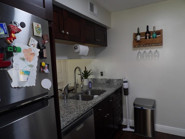 kitchen featuring light stone counters, dark wood-type flooring, sink, stainless steel appliances, and dark brown cabinetry