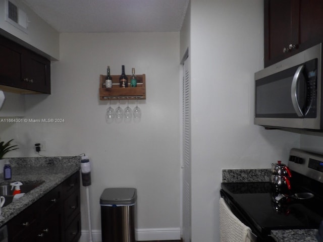 kitchen featuring dark brown cabinets, stove, light stone counters, and sink