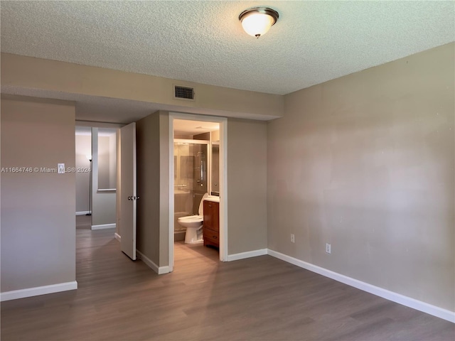 unfurnished bedroom featuring a textured ceiling, connected bathroom, and dark hardwood / wood-style flooring