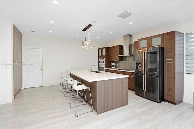 kitchen featuring visible vents, stainless steel appliances, light countertops, a kitchen bar, and wall chimney range hood