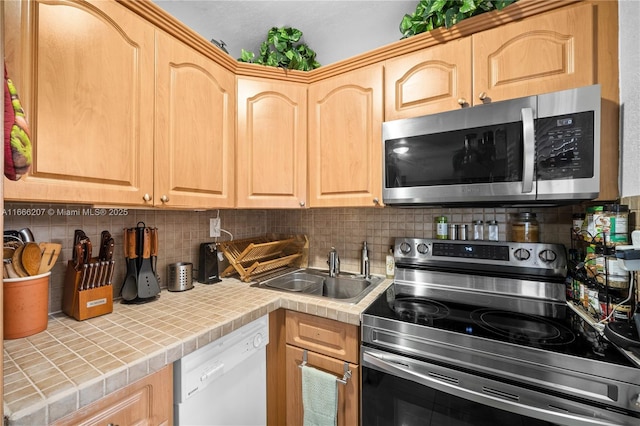 kitchen featuring light brown cabinets, a sink, appliances with stainless steel finishes, tile counters, and decorative backsplash