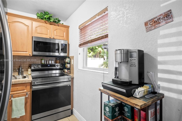 kitchen featuring tile countertops, stainless steel appliances, decorative backsplash, light brown cabinets, and baseboards