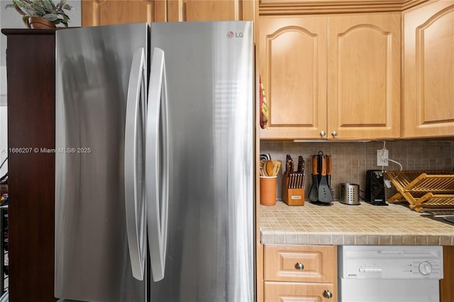kitchen with dishwasher, freestanding refrigerator, light brown cabinetry, backsplash, and tile countertops