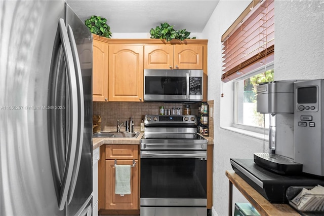kitchen with appliances with stainless steel finishes, light countertops, decorative backsplash, a sink, and light brown cabinetry