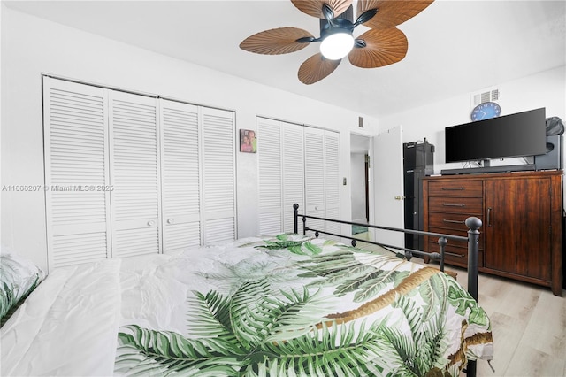 bedroom featuring visible vents, multiple closets, a ceiling fan, and light wood-style floors