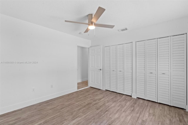 unfurnished bedroom featuring light wood-type flooring, ceiling fan, and multiple closets