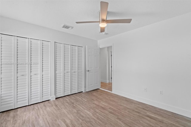 unfurnished bedroom featuring a textured ceiling, ceiling fan, multiple closets, and light hardwood / wood-style flooring