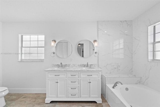 bathroom with a tub to relax in, vanity, toilet, and a wealth of natural light