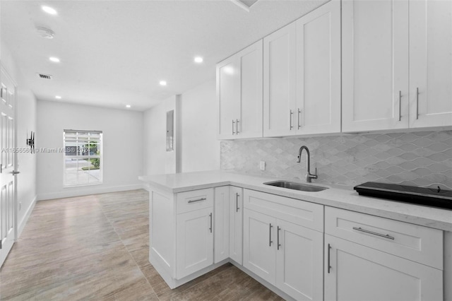 kitchen with decorative backsplash, light hardwood / wood-style floors, white cabinets, kitchen peninsula, and sink