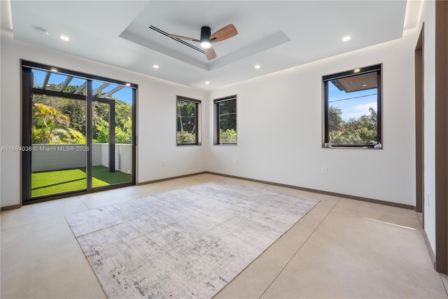 empty room with a healthy amount of sunlight, ceiling fan, and a tray ceiling