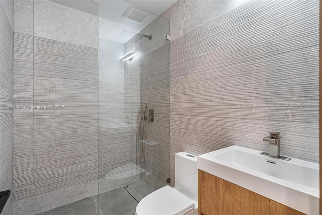 bathroom with tiled shower, vanity, toilet, and tile walls