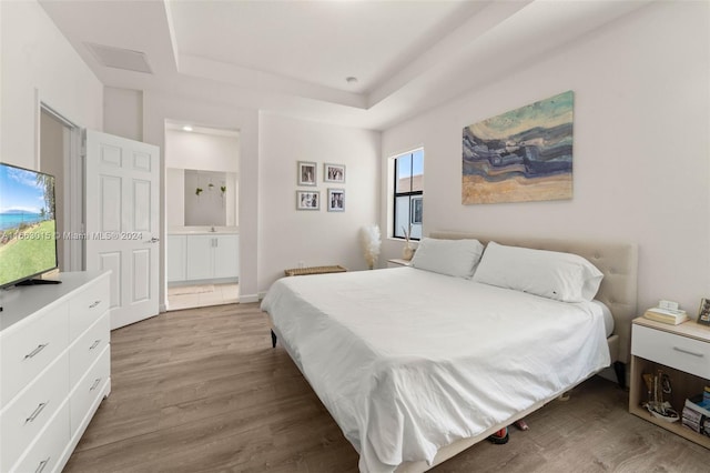 bedroom with hardwood / wood-style flooring, a raised ceiling, and ensuite bathroom