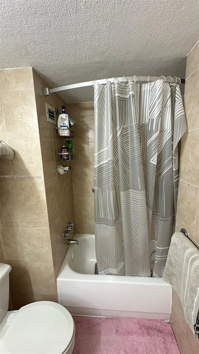 bathroom with a textured ceiling, tile walls, shower / bathtub combination with curtain, and toilet