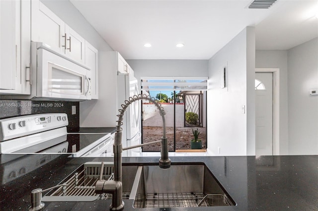 kitchen with white cabinets, dark stone counters, and white appliances