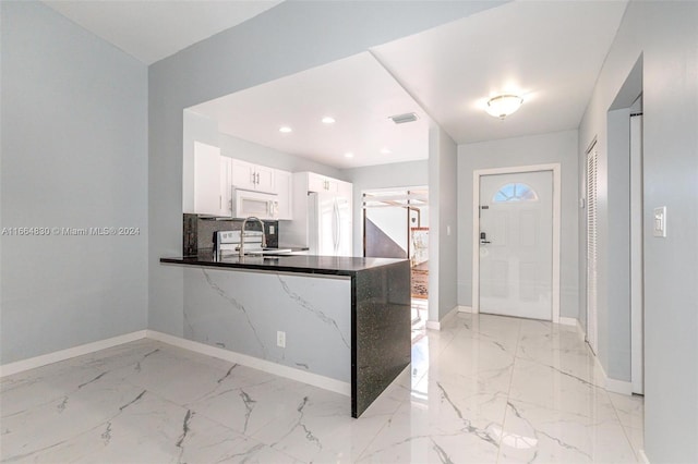 kitchen with white cabinets, sink, kitchen peninsula, white appliances, and dark stone countertops