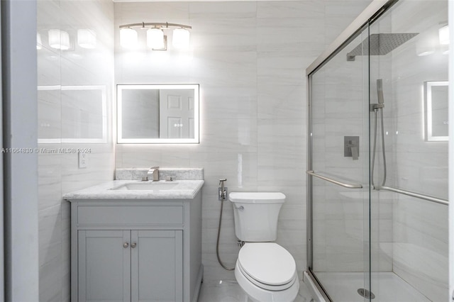 bathroom with tile walls, vanity, toilet, and an enclosed shower