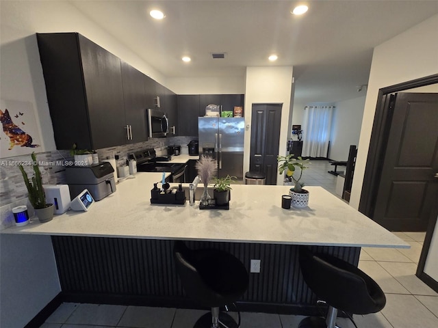 kitchen featuring kitchen peninsula, appliances with stainless steel finishes, a breakfast bar, and light tile patterned floors