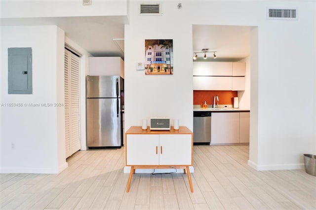 kitchen with appliances with stainless steel finishes, light wood-type flooring, electric panel, and white cabinets