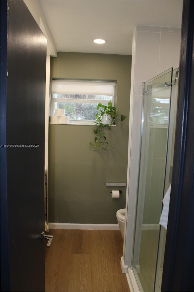 bathroom featuring hardwood / wood-style floors, toilet, and a shower with door