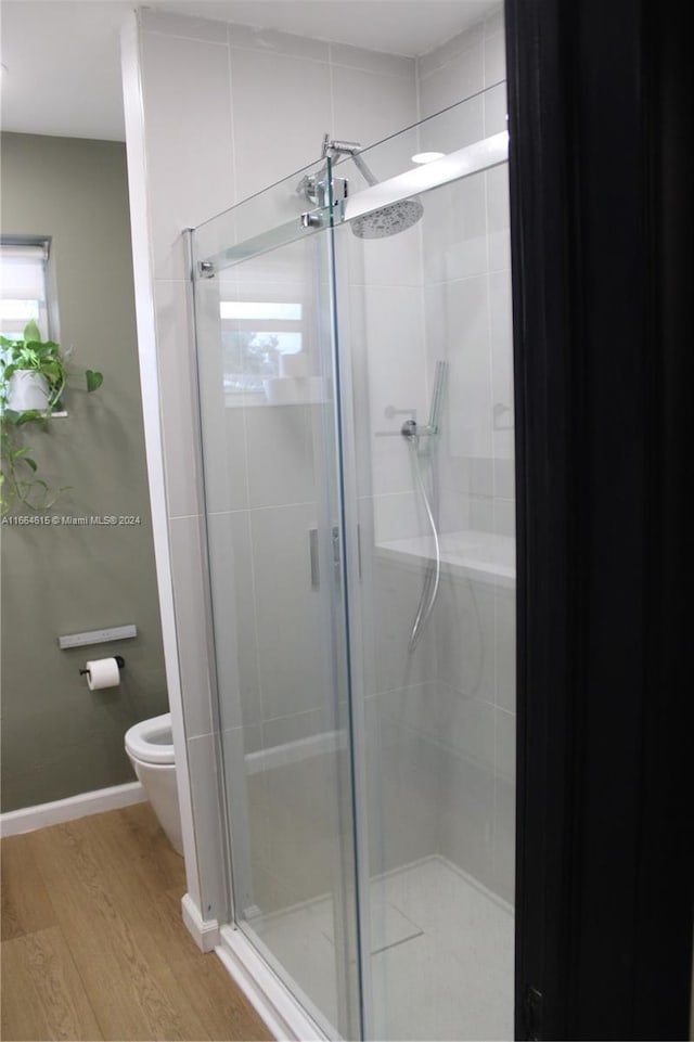 bathroom featuring wood-type flooring, a shower with shower door, and toilet