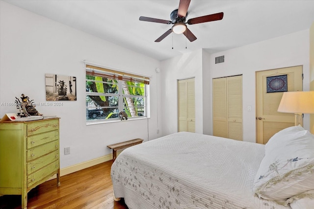 bedroom with wood-type flooring, two closets, and ceiling fan