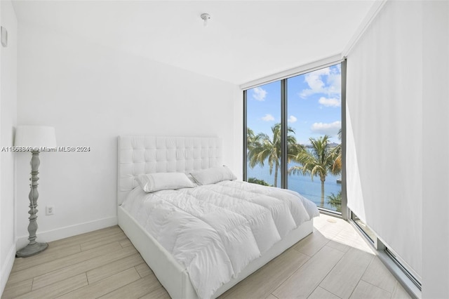 bedroom featuring a wall of windows, light wood-type flooring, and a water view