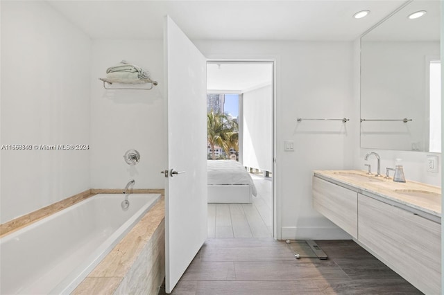 bathroom featuring hardwood / wood-style flooring, vanity, and a relaxing tiled tub