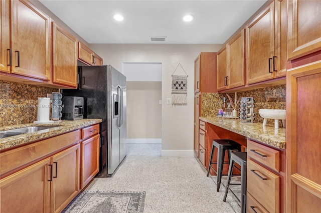 kitchen featuring light stone countertops, backsplash, and black fridge with ice dispenser