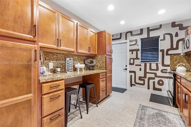 kitchen with light stone countertops, stainless steel appliances, built in desk, and decorative backsplash