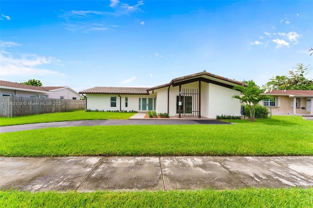 view of front of property with a yard, fence, a tiled roof, and stucco siding