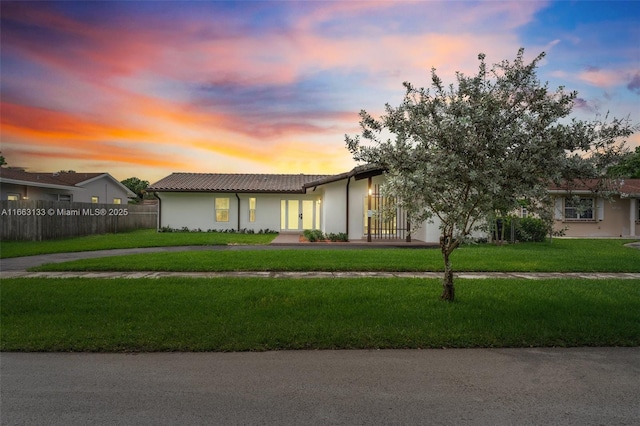 view of front of property featuring stucco siding, a tile roof, fence, and a front yard