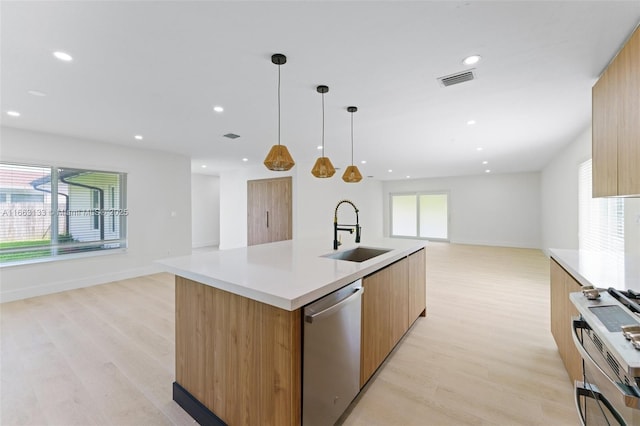 kitchen with an island with sink, open floor plan, a sink, light countertops, and stainless steel dishwasher