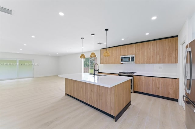 kitchen featuring a center island with sink, hanging light fixtures, stainless steel appliances, light countertops, and a sink