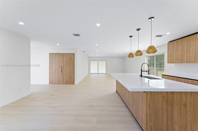 kitchen featuring a spacious island, modern cabinets, light countertops, pendant lighting, and a sink