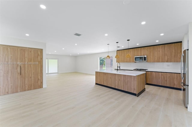 kitchen with modern cabinets, appliances with stainless steel finishes, a kitchen island with sink, light countertops, and pendant lighting