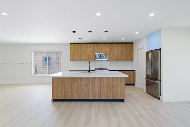 kitchen with stainless steel appliances, hanging light fixtures, light countertops, and a center island with sink