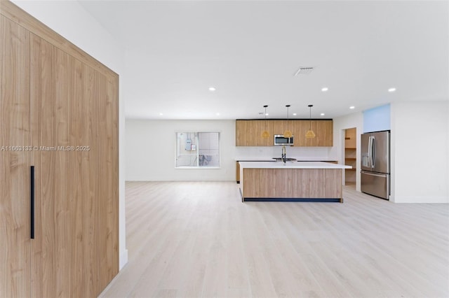 kitchen featuring light countertops, hanging light fixtures, appliances with stainless steel finishes, an island with sink, and modern cabinets