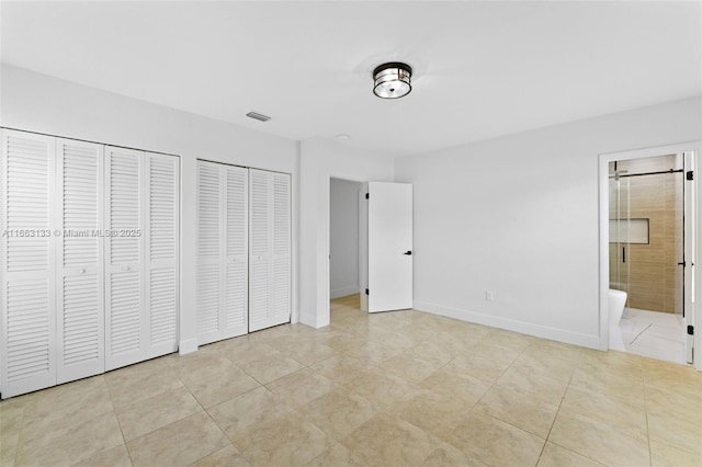 unfurnished bedroom featuring multiple closets, light tile patterned flooring, ensuite bath, and baseboards