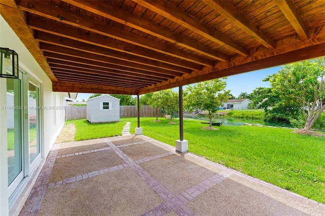 view of patio / terrace featuring a water view, a storage shed, a fenced backyard, and an outdoor structure