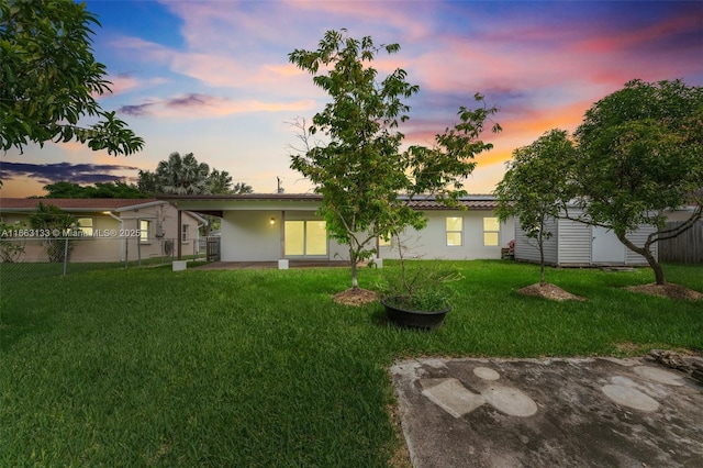 back of property at dusk featuring a yard, a patio, fence, and stucco siding