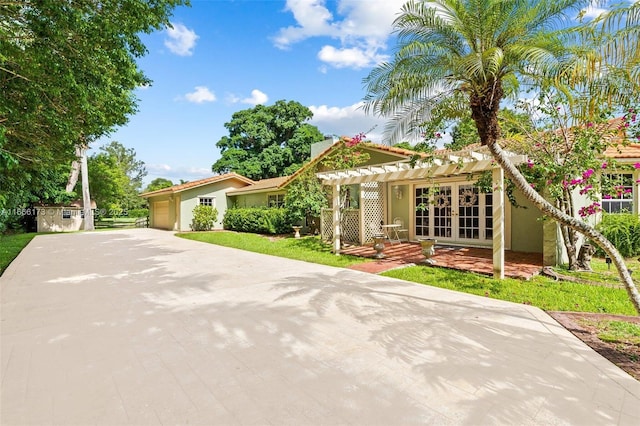 view of front of house featuring a storage unit, a pergola, a garage, a front lawn, and french doors