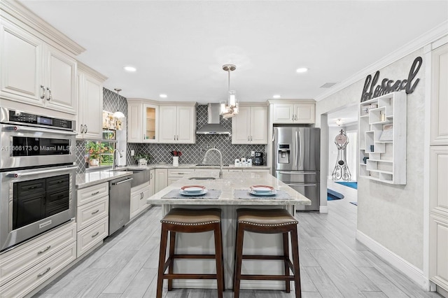 kitchen with appliances with stainless steel finishes, wall chimney range hood, hanging light fixtures, a kitchen island with sink, and light stone counters