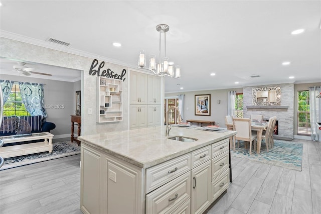 kitchen featuring sink, decorative light fixtures, light wood-type flooring, ornamental molding, and light stone counters