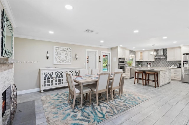 dining area with a fireplace, light hardwood / wood-style floors, sink, and ornamental molding