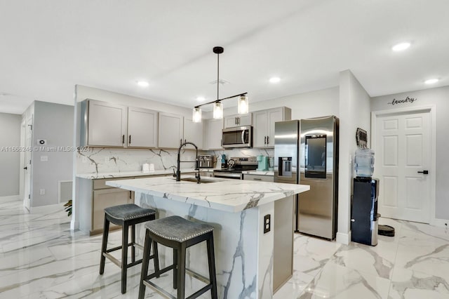 kitchen with pendant lighting, sink, a kitchen island with sink, stainless steel appliances, and light stone countertops