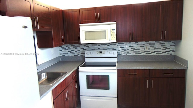 kitchen with a sink, dark countertops, backsplash, white appliances, and reddish brown cabinets